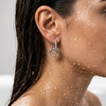 Close-up of a person wearing silver hoop earrings with water droplets on skin and hair.