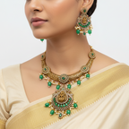 Woman wearing a gold and green jewelry set with a beige saree on a light gray background