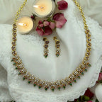 Gold-plated floral necklace and earrings set with crystal florals and green drops, styled with candles and rose petals