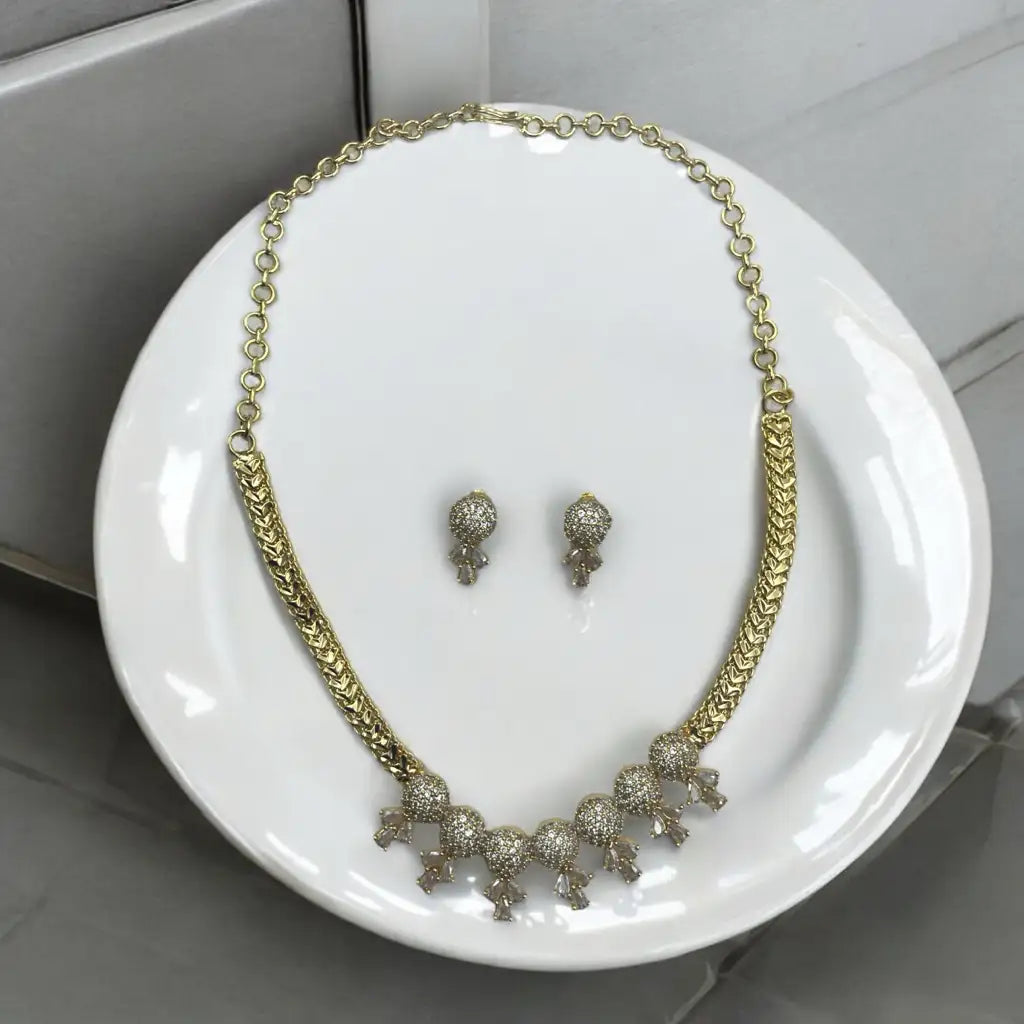 Gold-plated crystal necklace and matching stud earrings with pave clusters and drops, flat-lay on a white plate