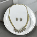 Gold-plated crystal necklace and matching stud earrings with pave clusters and drops, flat-lay on a white plate