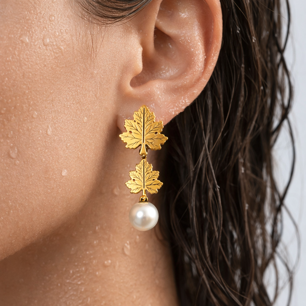 Gold leaf earrings with a pearl drop worn by a person.
