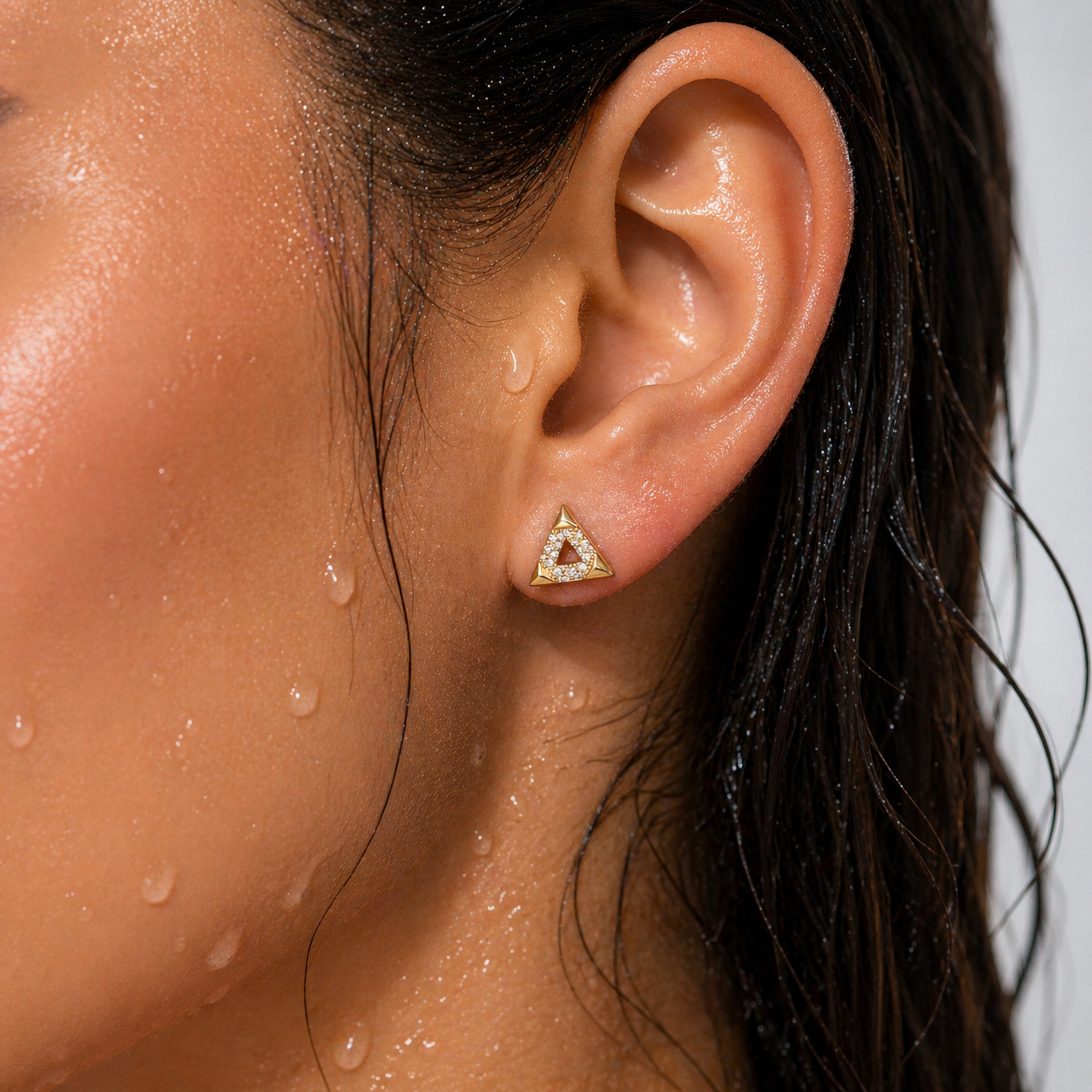 Close-up of an ear wearing a triangular earring with a red gemstone, against a blurred background.