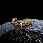 Gold bracelet with black patterns on a dark, textured surface