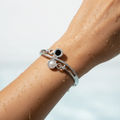 Silver bracelet with black and pearl accents on a wet arm against a light background