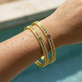Gold crystal bangle set with green and pink gemstone accents, pair stacked on wrist