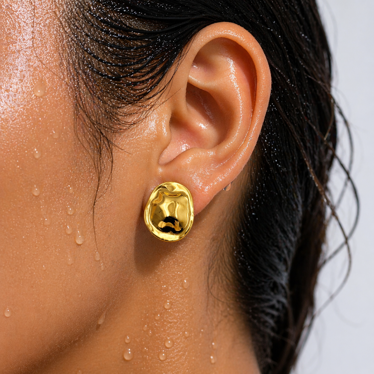 Close-up of an ear wearing a gold earring with a white background