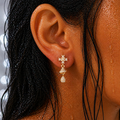 Close-up of an ear wearing a gold earring with a cross design, surrounded by wet hair.