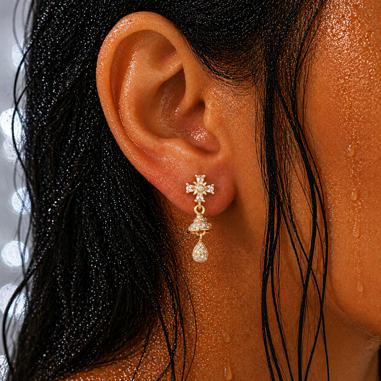 Close-up of an ear wearing a gold earring with a cross design, surrounded by wet hair.