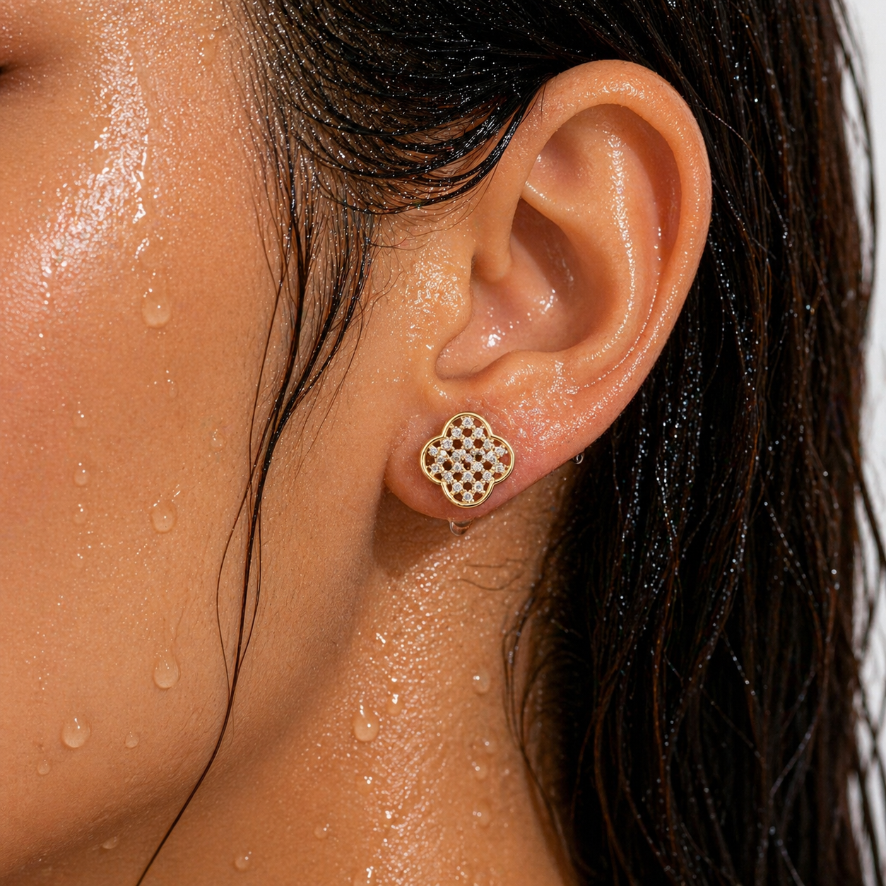 Close-up of an ear wearing a gold earring with water droplets on skin
