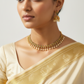 Woman wearing a gold necklace and earrings with a beige saree on a light background