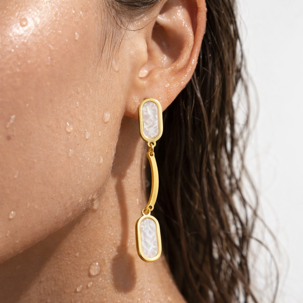 Golden earring with a white stone worn by a person with water droplets on skin
