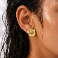 Close-up of an ear wearing a gold flower earring with wet hair.