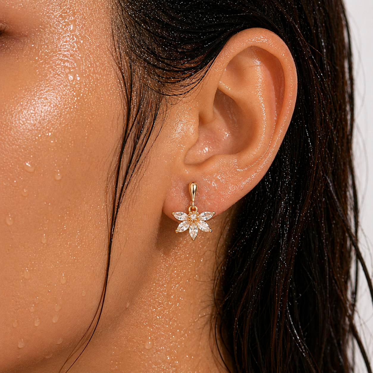 Close-up of an ear wearing a gold flower-shaped earring with clear stones.