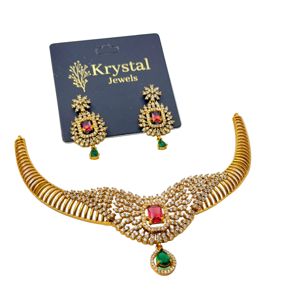 Woman wearing a gold necklace with red and green gemstones on a plain background