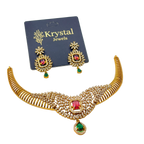 Woman wearing a gold necklace with red and green gemstones on a plain background