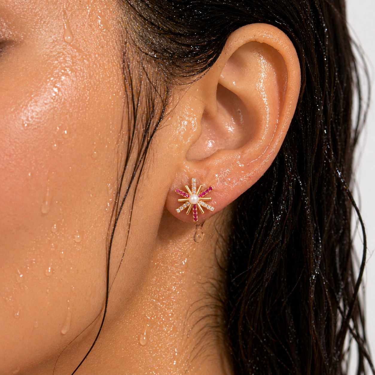 Close-up of an ear wearing a decorative earring with water droplets on skin