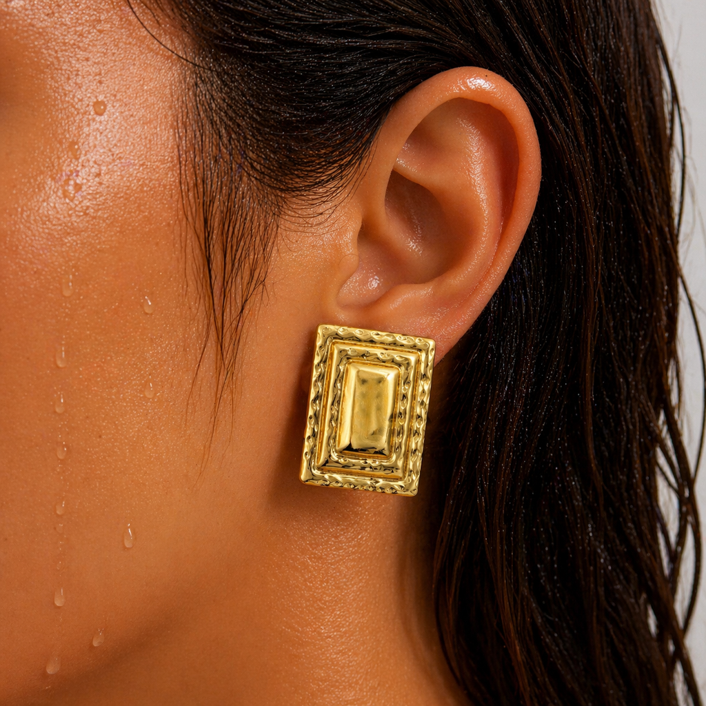 Gold-tone tiered frame stud earring, textured border close-up worn on ear