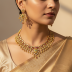 Woman wearing a gold necklace and earrings with a beige saree against a neutral background