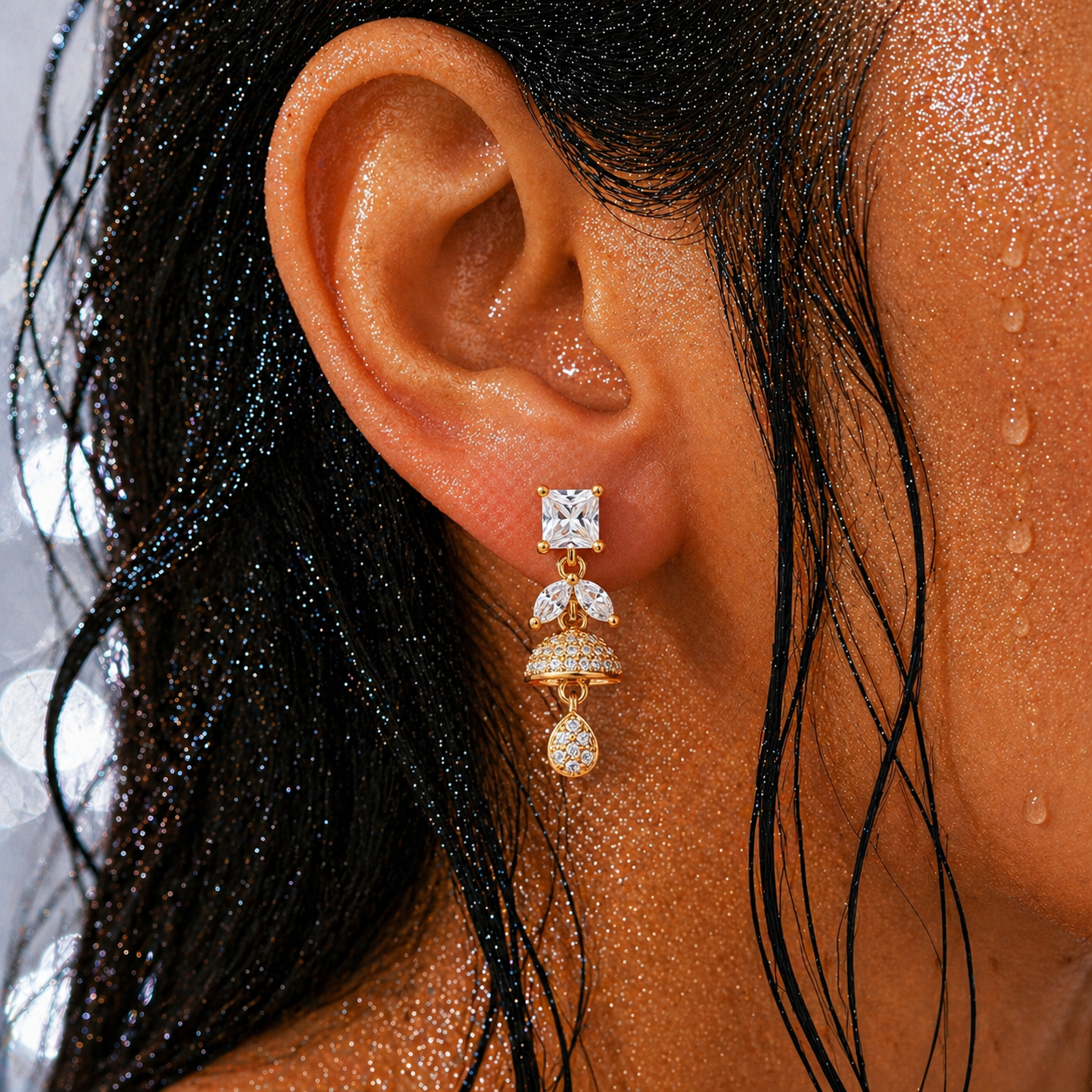 Close-up of an ear wearing a gold and diamond earring with water droplets on skin and hair.