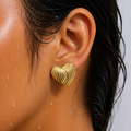 Close-up of an ear wearing a gold heart-shaped earring with water droplets on skin.