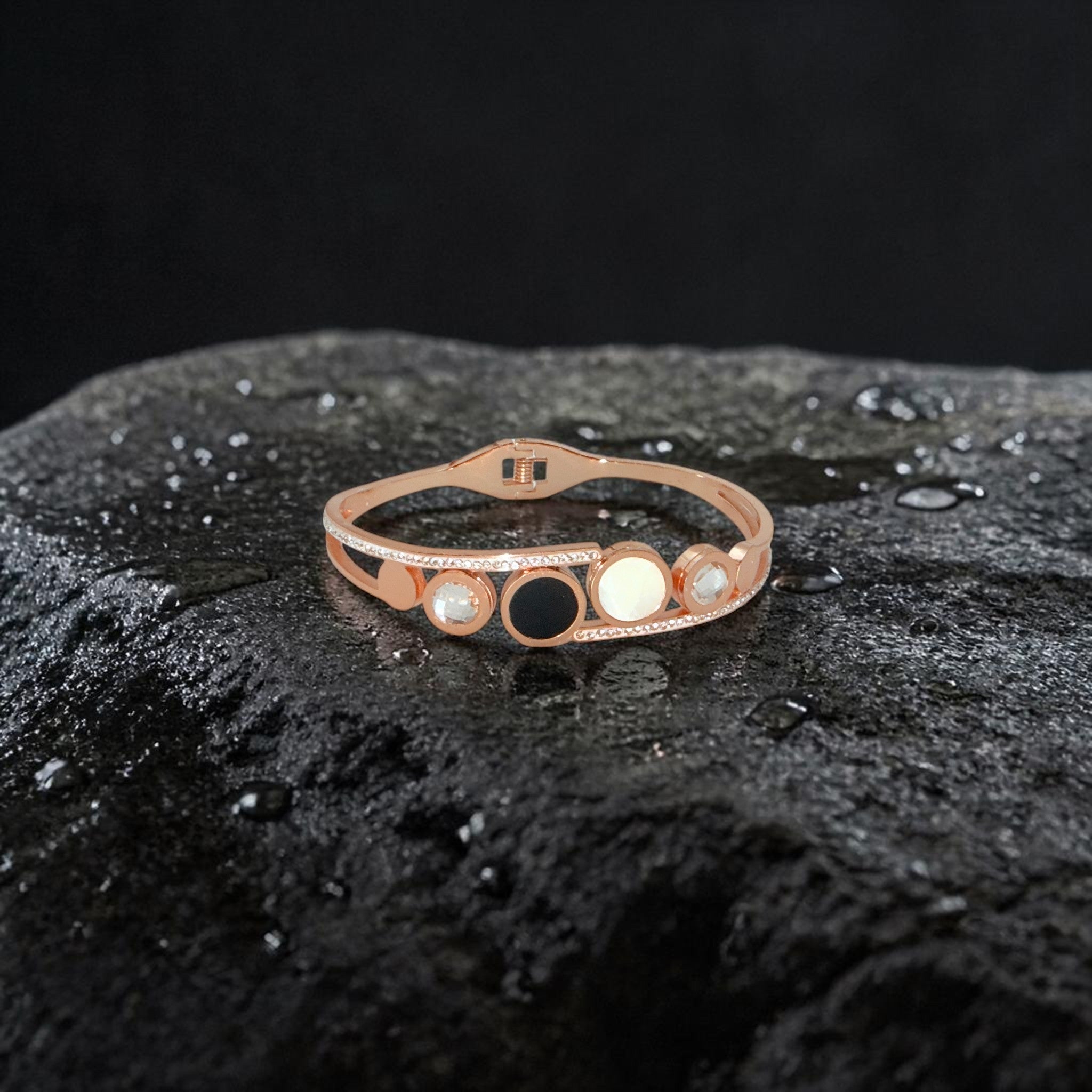 Rose gold bracelet with black and white stones on a dark textured surface