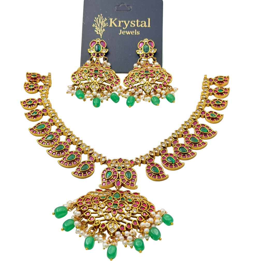 Woman wearing a gold necklace and earrings with green gemstones on a plain background