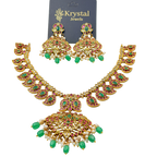 Woman wearing a gold necklace and earrings with green gemstones on a plain background