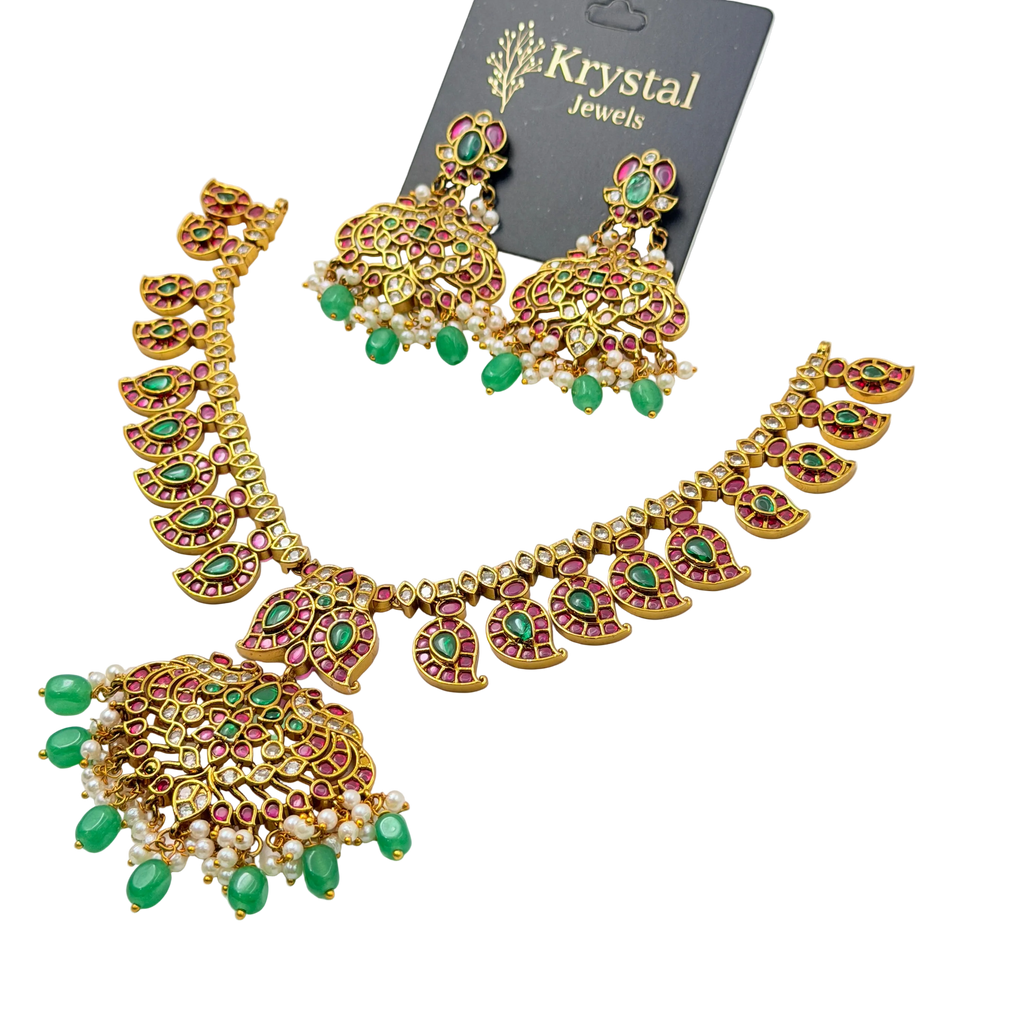 Ornate necklace and earrings set with green and red stones on a clear background, branded 'Krystal Jewels'.
