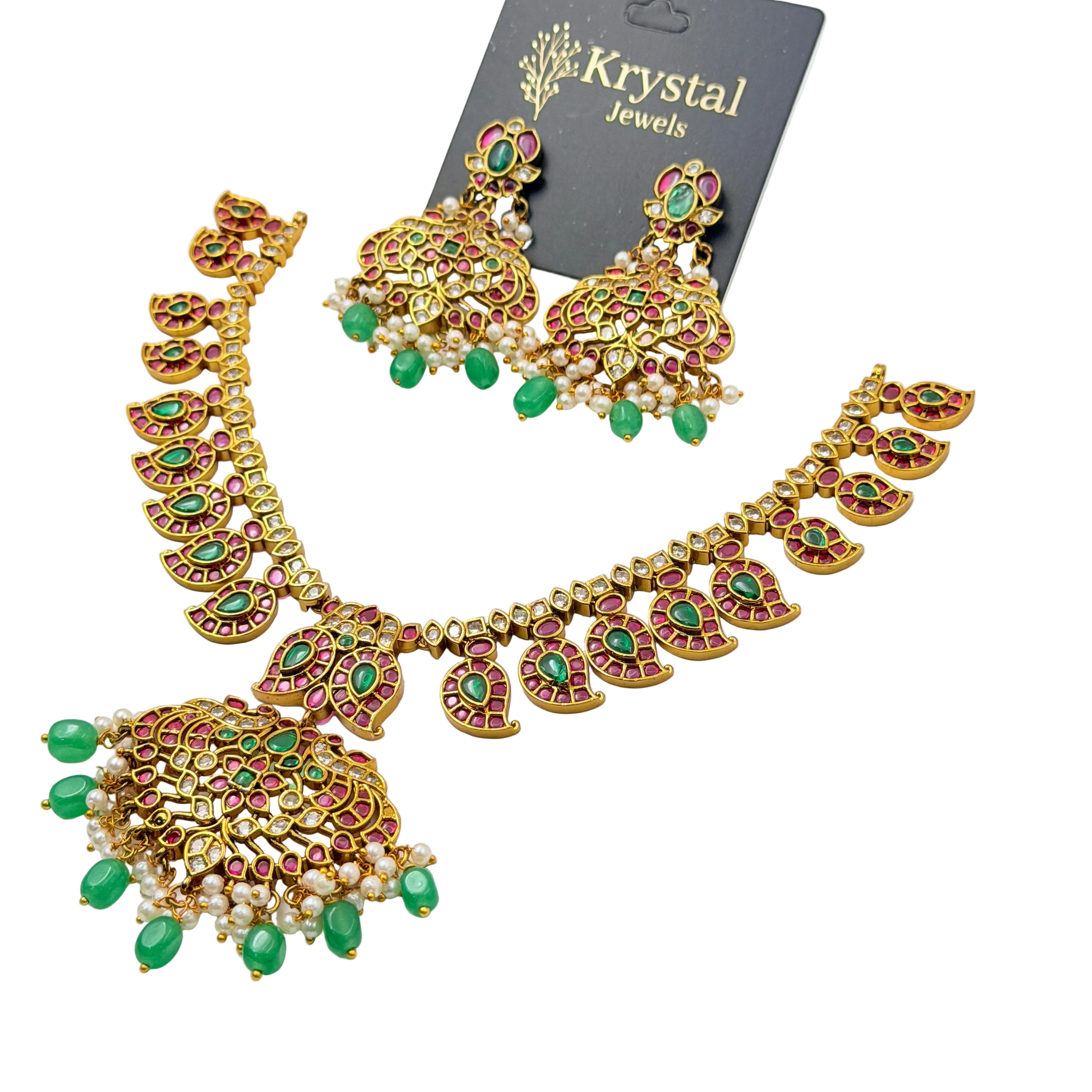 Ornate necklace and earrings set with green and red stones on a clear background, branded 'Krystal Jewels'.