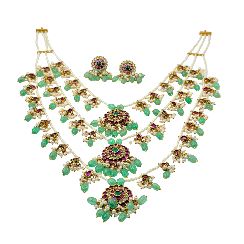 Ornate necklace and earrings set with green stones on a white background
