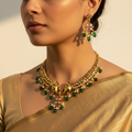 Woman wearing gold jewelry with green and red stones against a neutral background