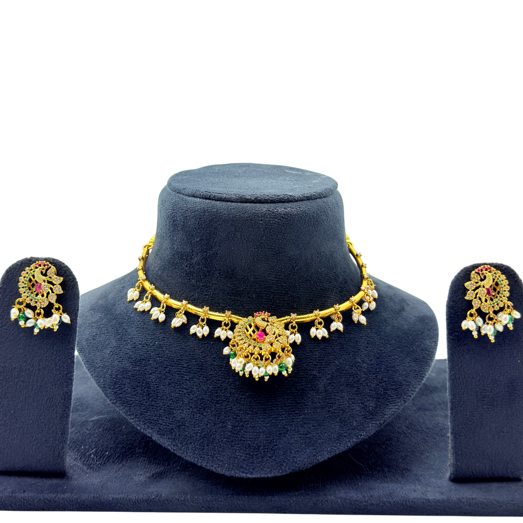 Gold necklace with pearl and gemstone details on a blue stand, accompanied by matching earrings.