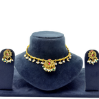 Gold necklace with pearl and gemstone details on a blue stand, accompanied by matching earrings.