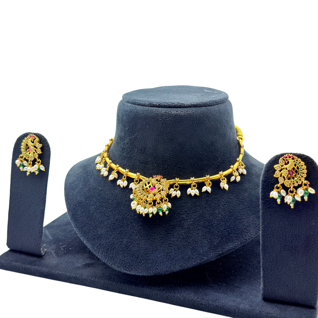Gold necklace with floral designs and matching earrings on a blue stand against a white background