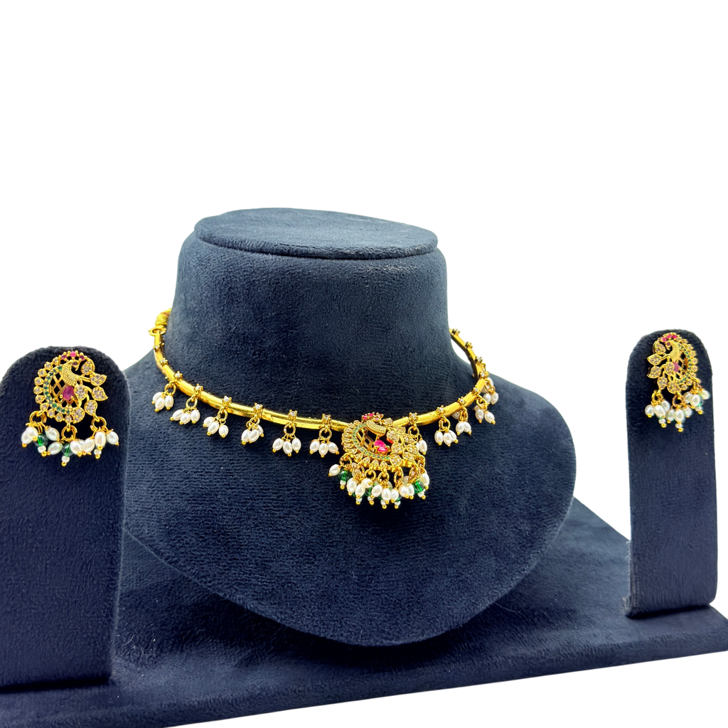 Gold necklace and earrings set on a blue velvet stand with a white background