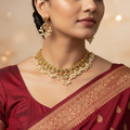 Woman wearing a gold necklace and earrings with a maroon saree against a warm-toned background