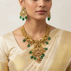 Woman wearing gold jewelry with green stones on a plain background
