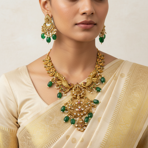 Woman wearing gold jewelry with green stones on a plain background