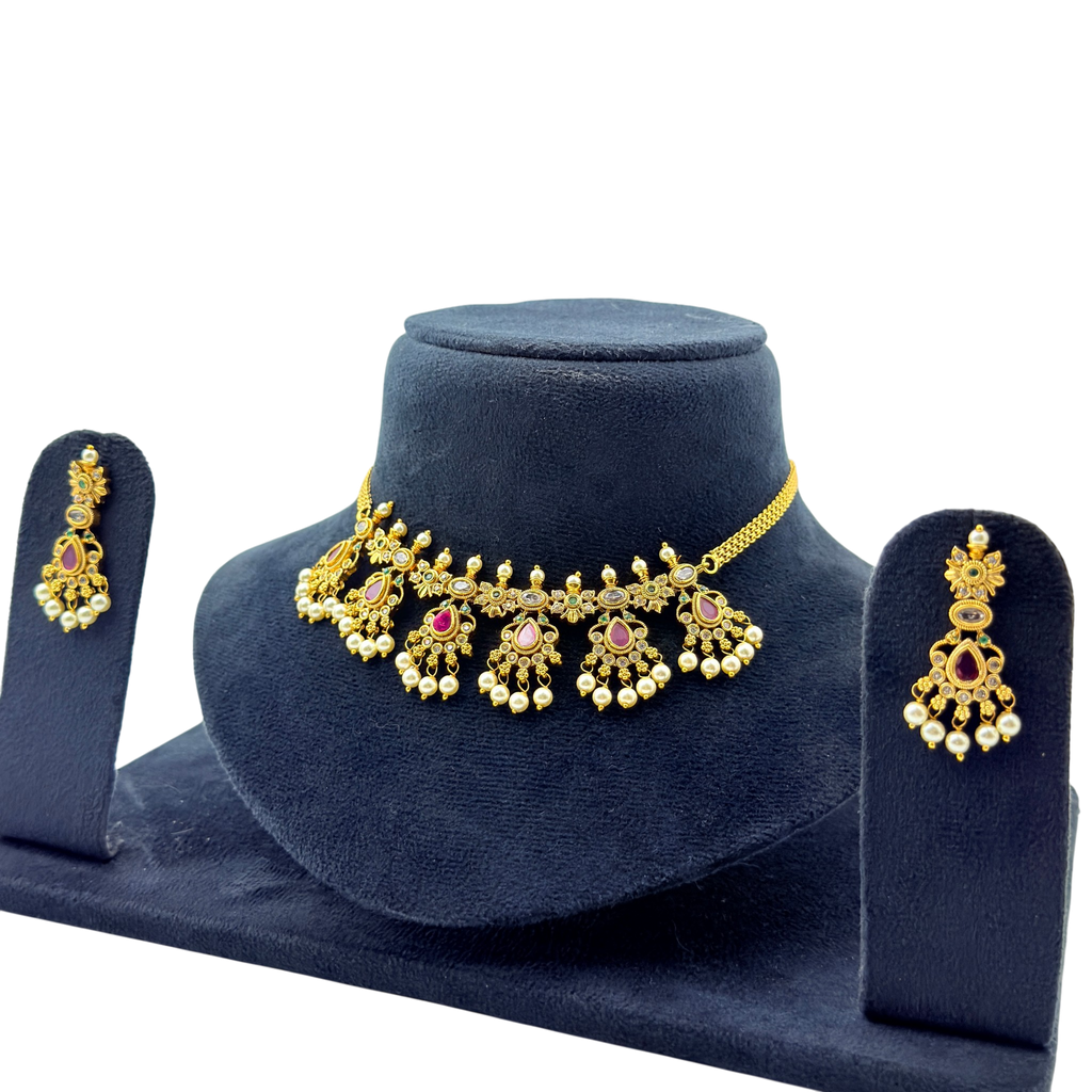 Gold necklace and earrings set on a blue velvet stand with a white background