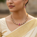 Woman wearing a gold necklace with pink gemstones and matching earrings.