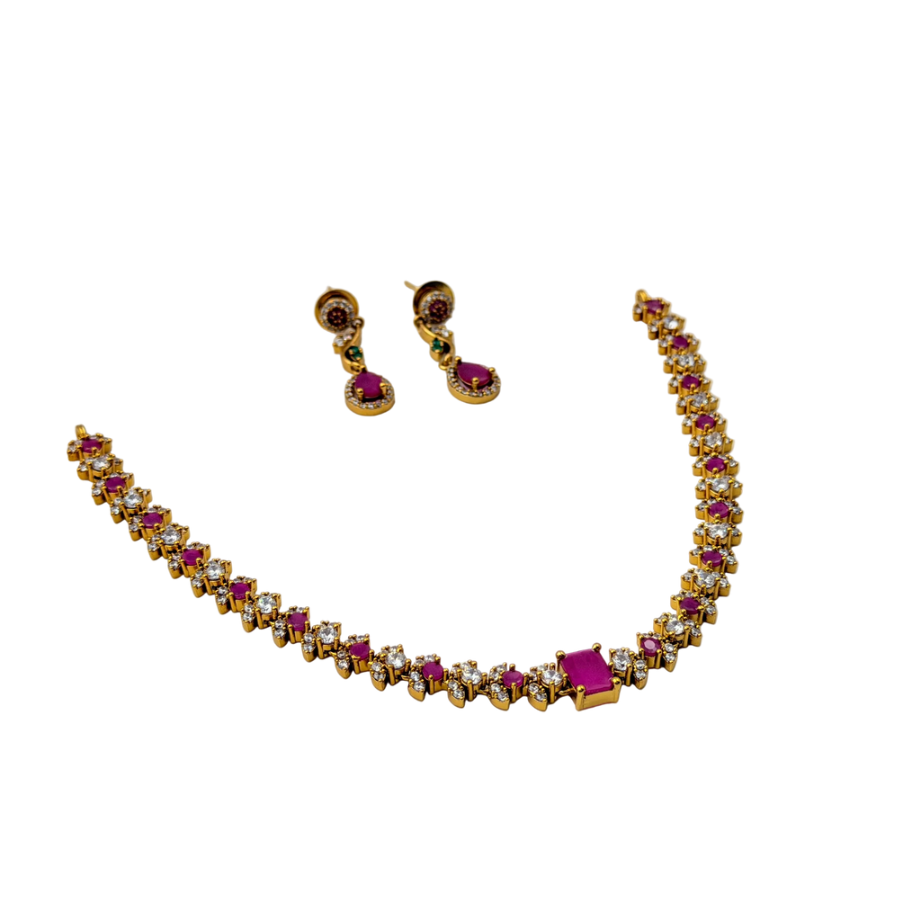 Gold necklace with red and clear gemstones and matching earrings on a white background