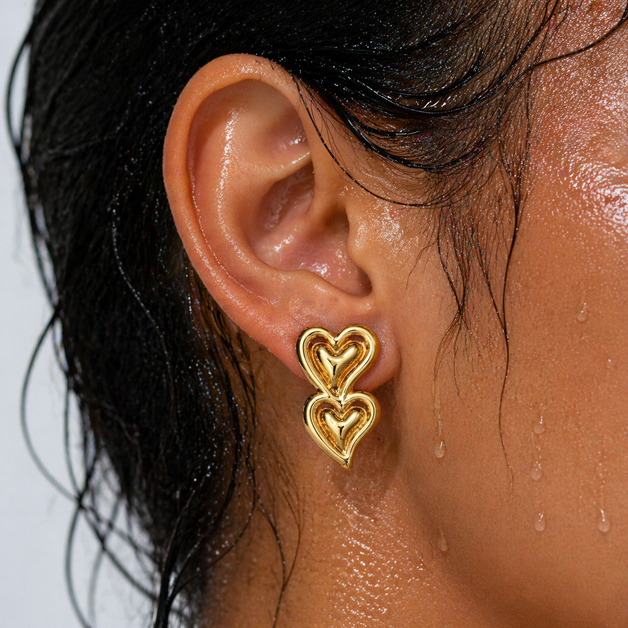 Close-up of an ear wearing a gold heart-shaped earring with a blurred background.