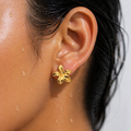 Close-up of an ear wearing a gold flower-shaped earring with a blurred background