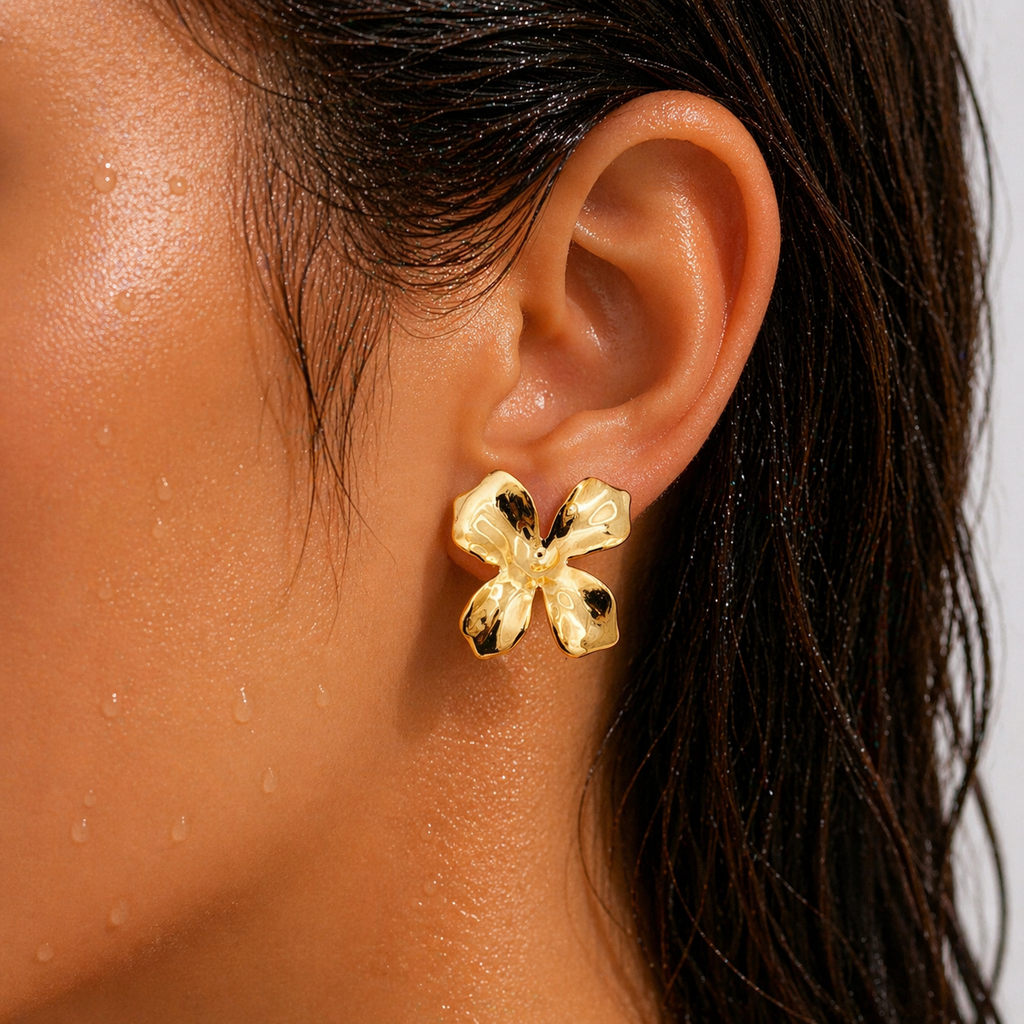 Gold-tone sculptural molten orchid stud earring worn on ear, close-up showing mirror-shine four-petal design