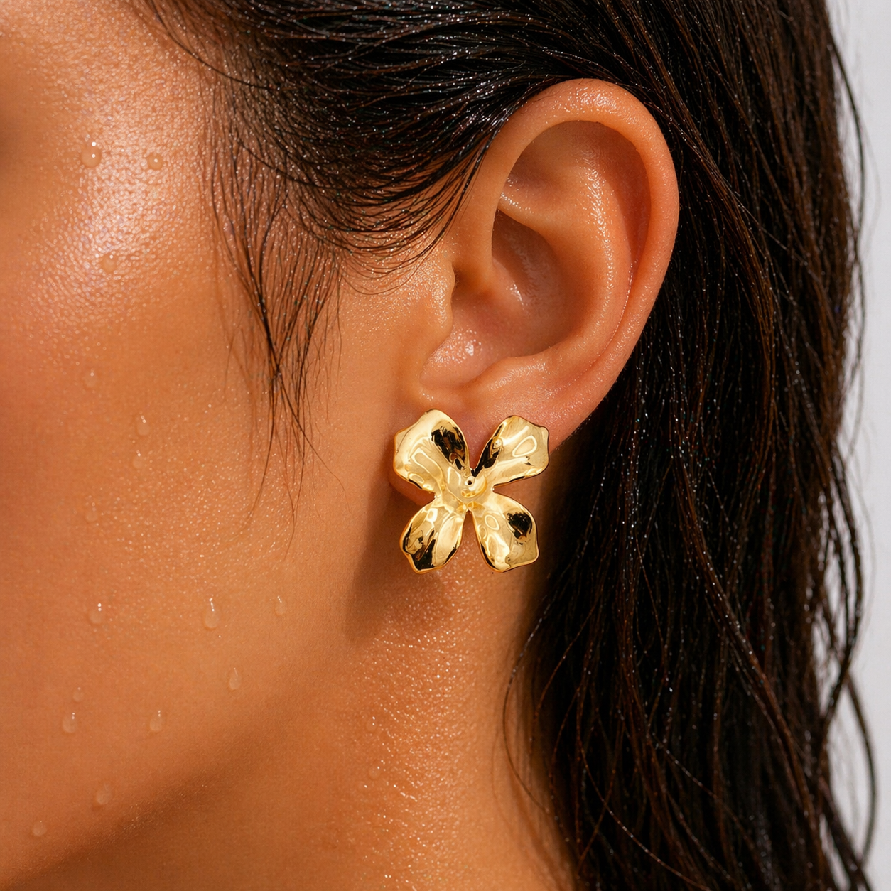 Golden earrings worn by a person with dark hair and skin.