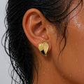 Close-up of an ear wearing a gold earring with water droplets on skin and hair.