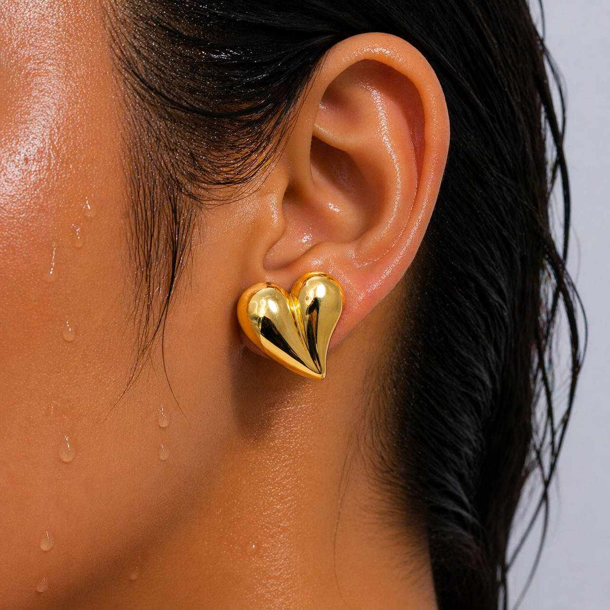 Gold heart-shaped earring worn by a person with wet hair.