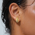 Close-up of an ear wearing a gold earring with water droplets on skin and hair.