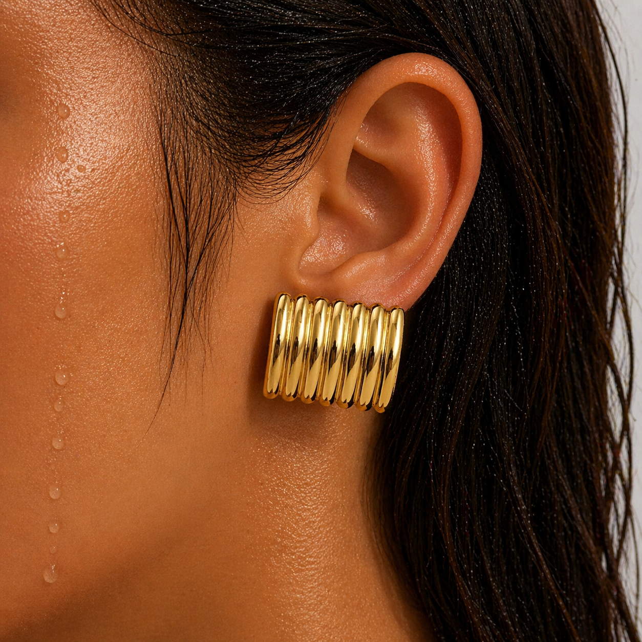 Gold hoop earrings worn by a person with dark hair.